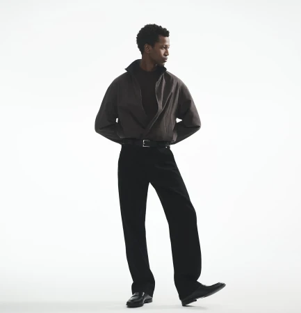 Man wearing a dark jacket and black trousers against a white seamless background for Theory fall 2025 campaign.