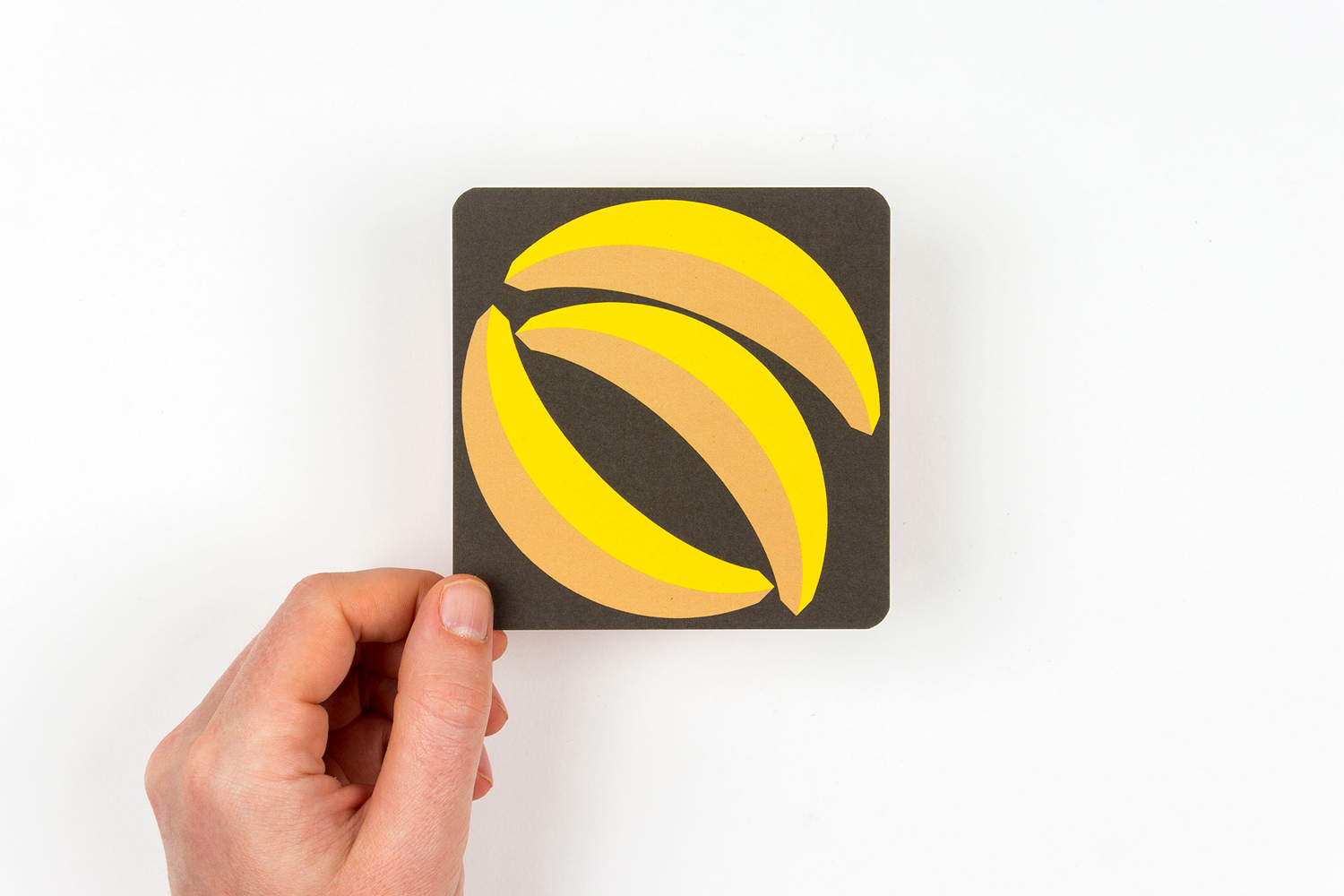 Hand holding a square graphic card featuring yellow and brown stylized banana illustrations on a black background