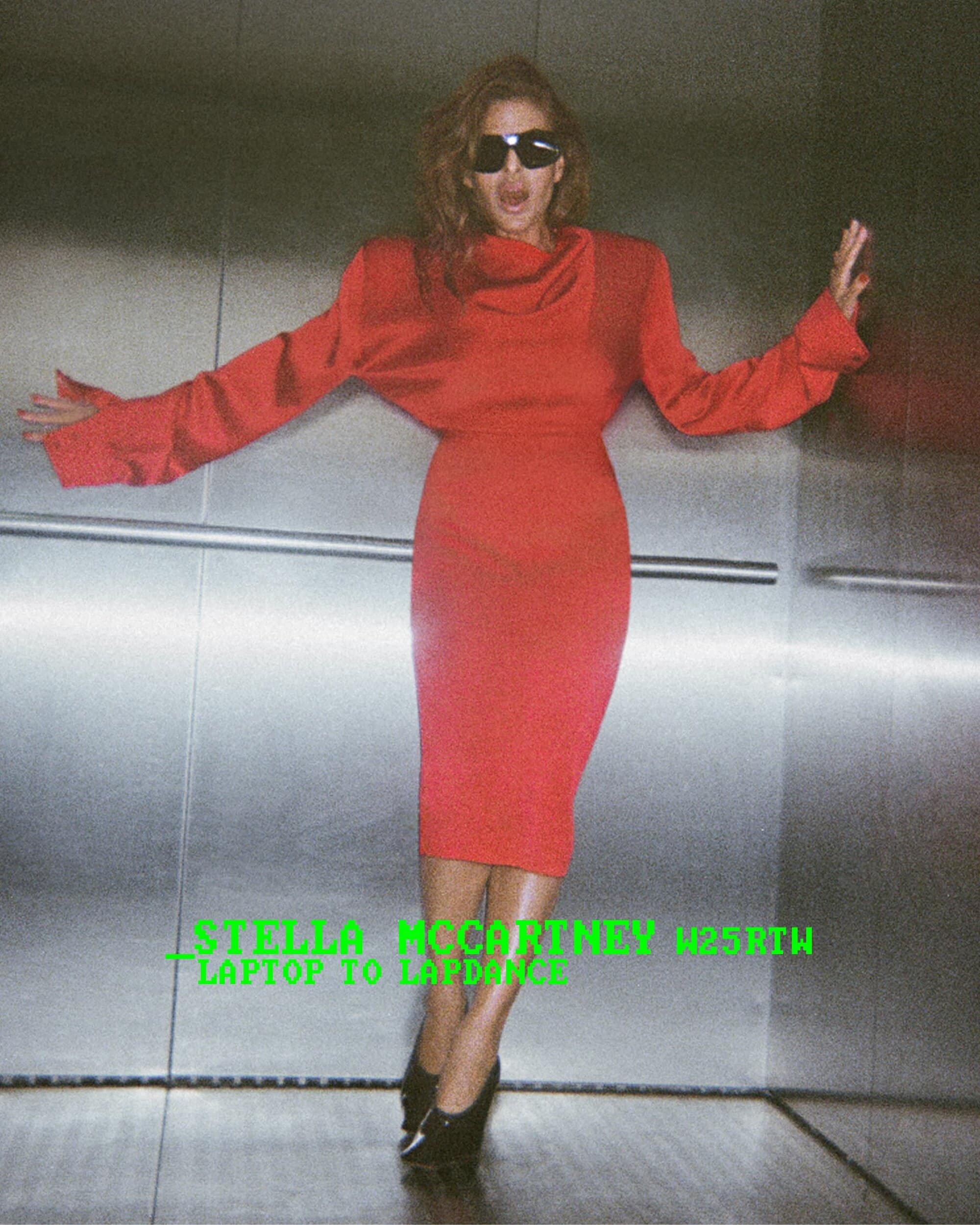 Model wearing a bright red dress and sunglasses inside an elevator with metal paneling for Stella McCartney.