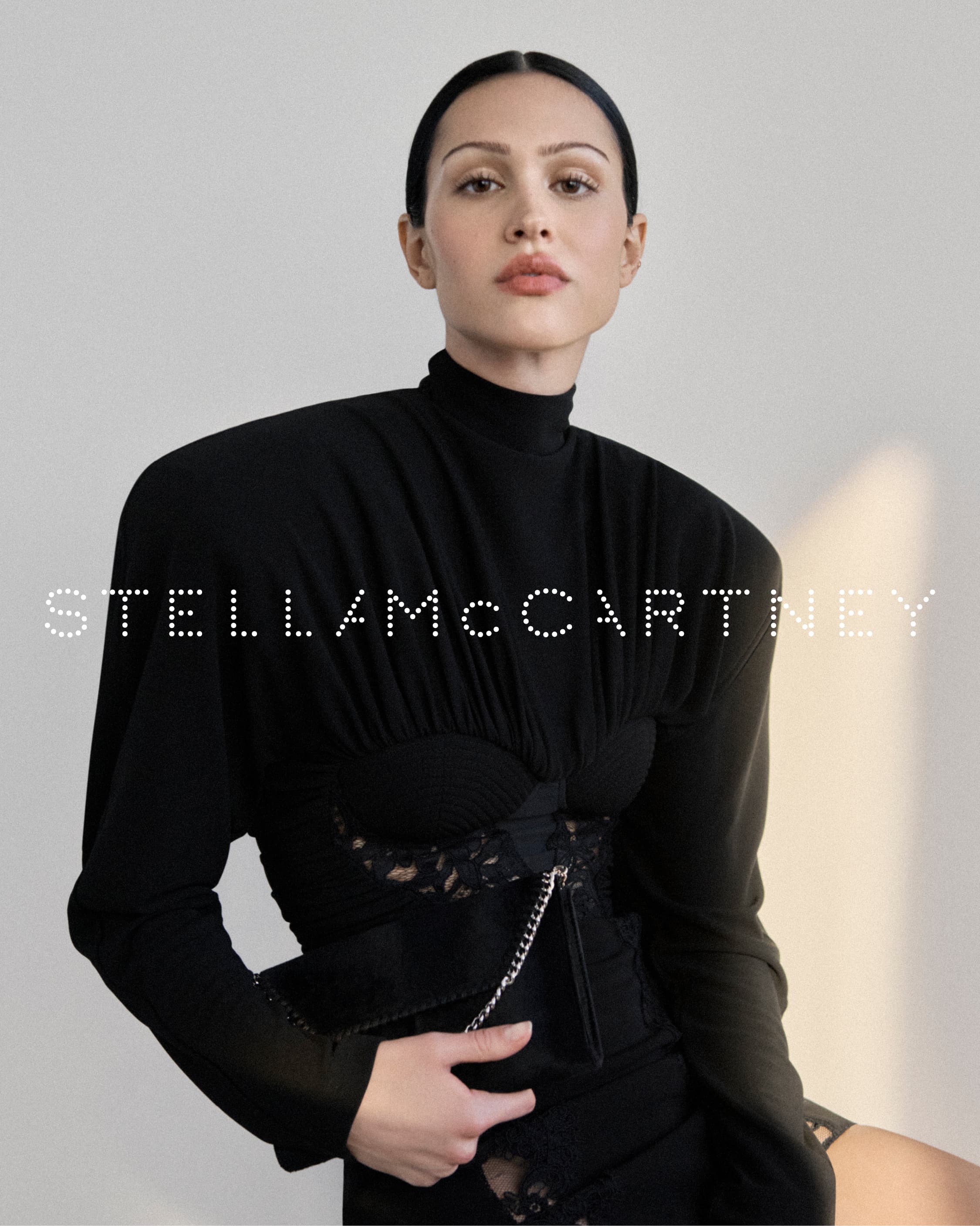 Amelia Gray wearing a black structured top against a plain studio background for Stella McCartney Winter 2025 ad campaign.