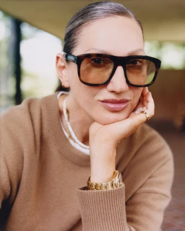 Jenna Lyons wearing oversized tortoiseshell sunglasses and a camel sweater with a gold watch and pearl necklace for Aritzia.