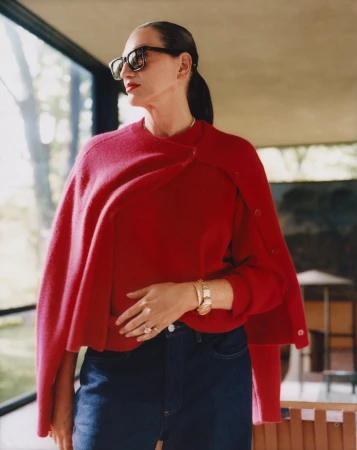 Jenna Lyons wearing sunglasses and a red sweater over her shoulders with blue jeans in a modern interior.