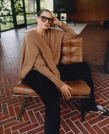 Jenna Lyons seated in a tan sweater and black pants on a brown leather armchair for Aritzia Fall 2025 campaign