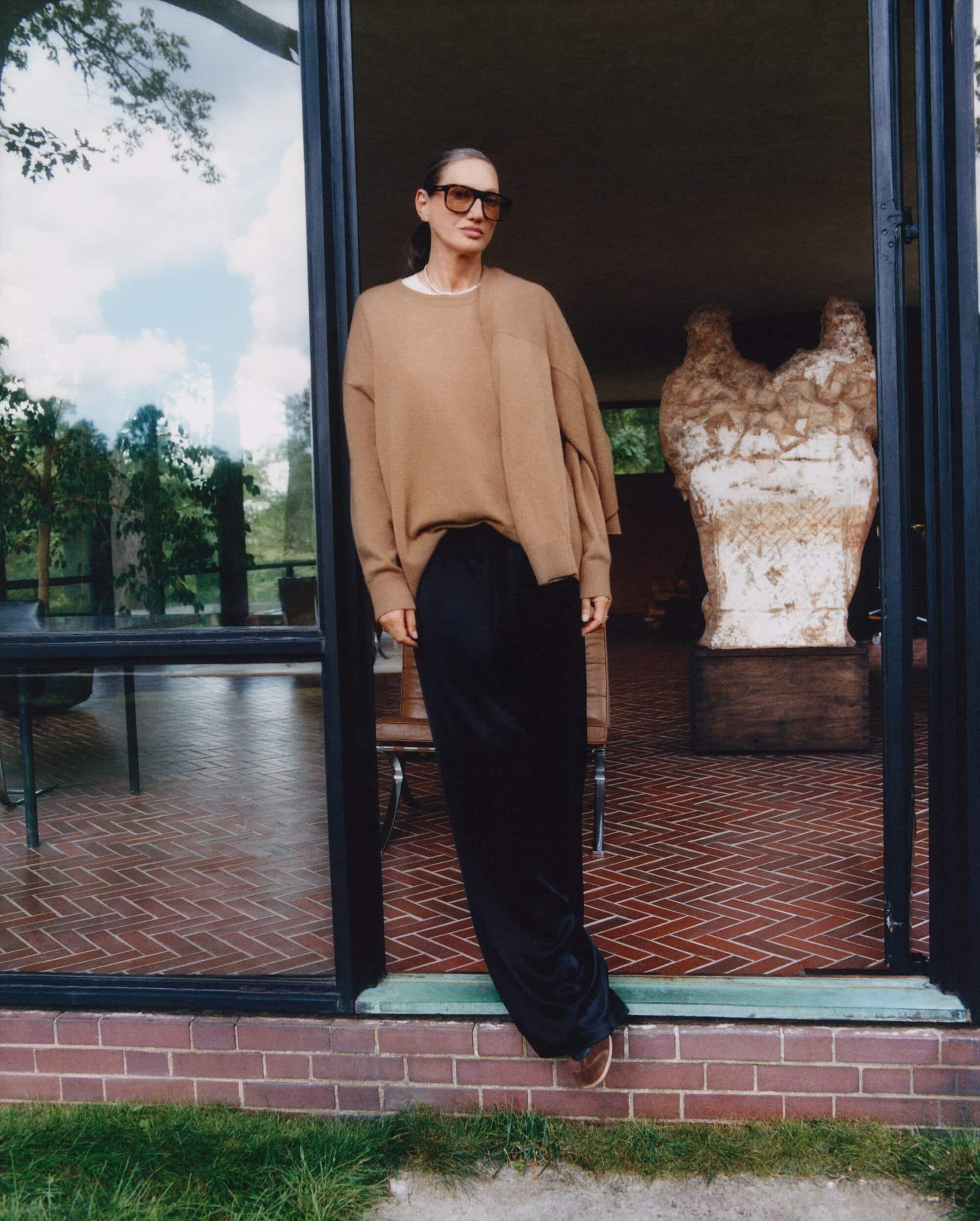 Jenna Lyons wearing brown sweater and black pants standing in a doorway for Aritzia Fall 2025 ad campaign.