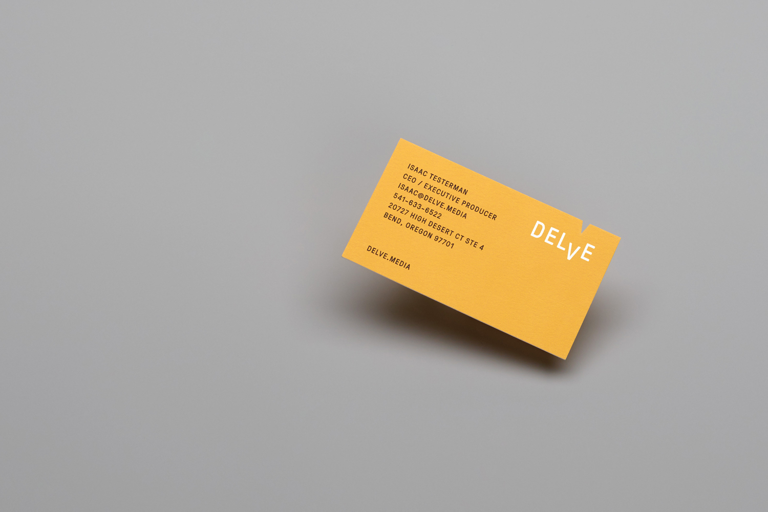Yellow business card featuring Delve branding placed diagonally on a smooth neutral grey background