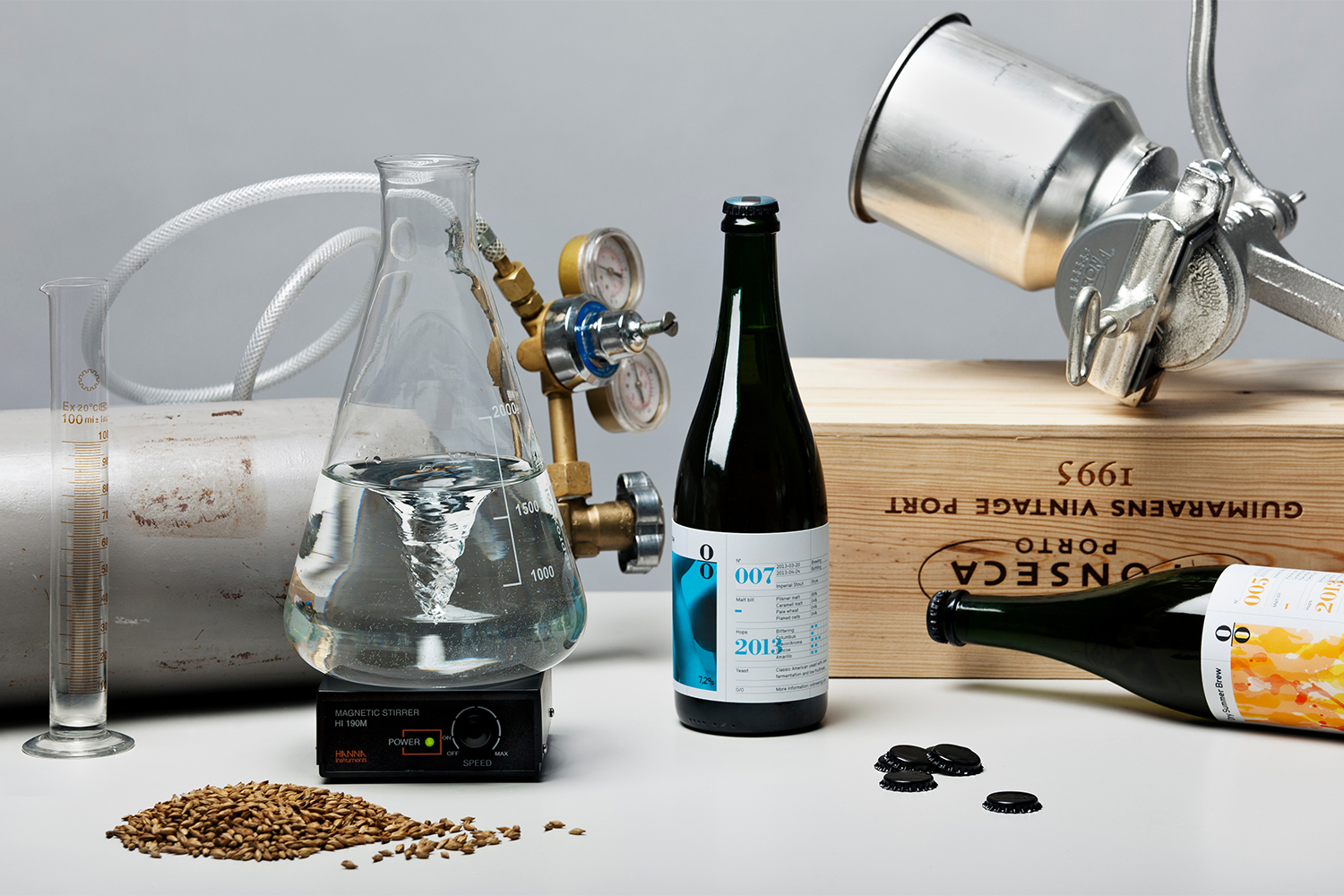 Glass Erlenmeyer flask with swirling liquid, green beer bottles, and laboratory equipment on a grey surface.