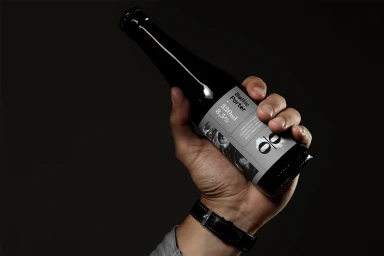 Hand holding a dark glass beer bottle with a grey label against a dark background