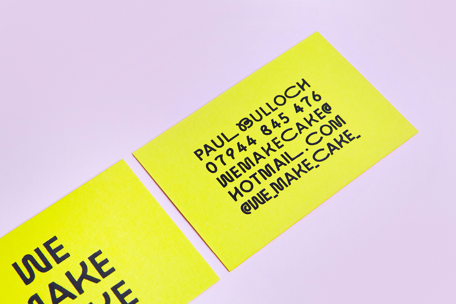 Two bright yellow business cards with black typography placed diagonally on a smooth light purple background.