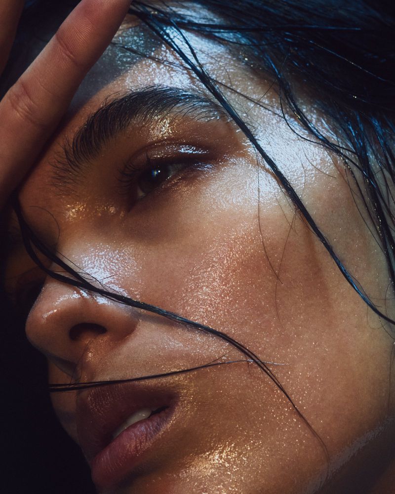 Close-up portrait of a woman with wet skin and hair against a dark background, highlighting her facial features and natural beauty.