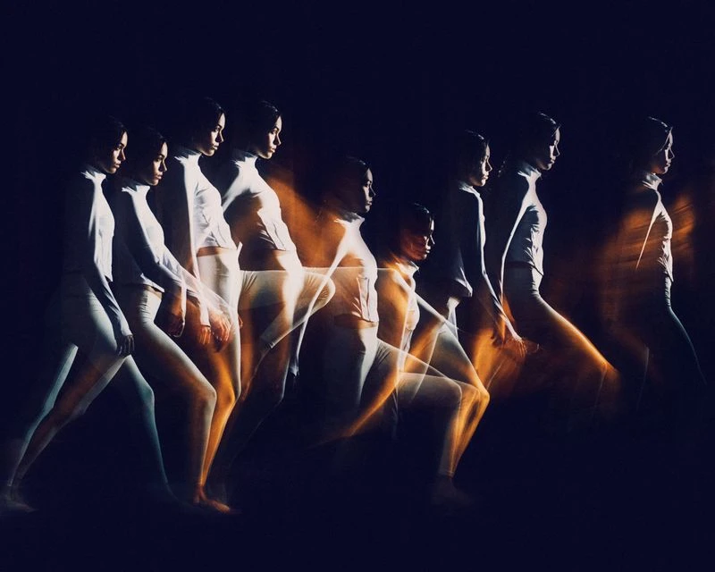 Multiple exposure shot of a woman in white athletic wear walking. High key image against dark background, motion blur and repetition.