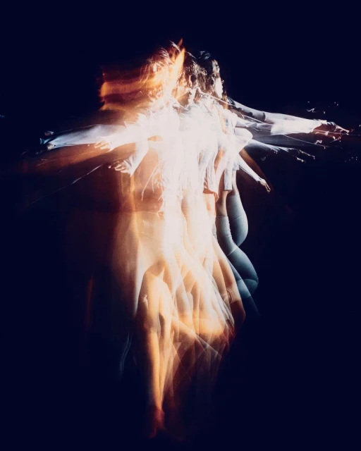 Multiple exposure photo of a woman with motion blur effect, dressed in white in a dark indoor setting, creating an ethereal, dynamic image.