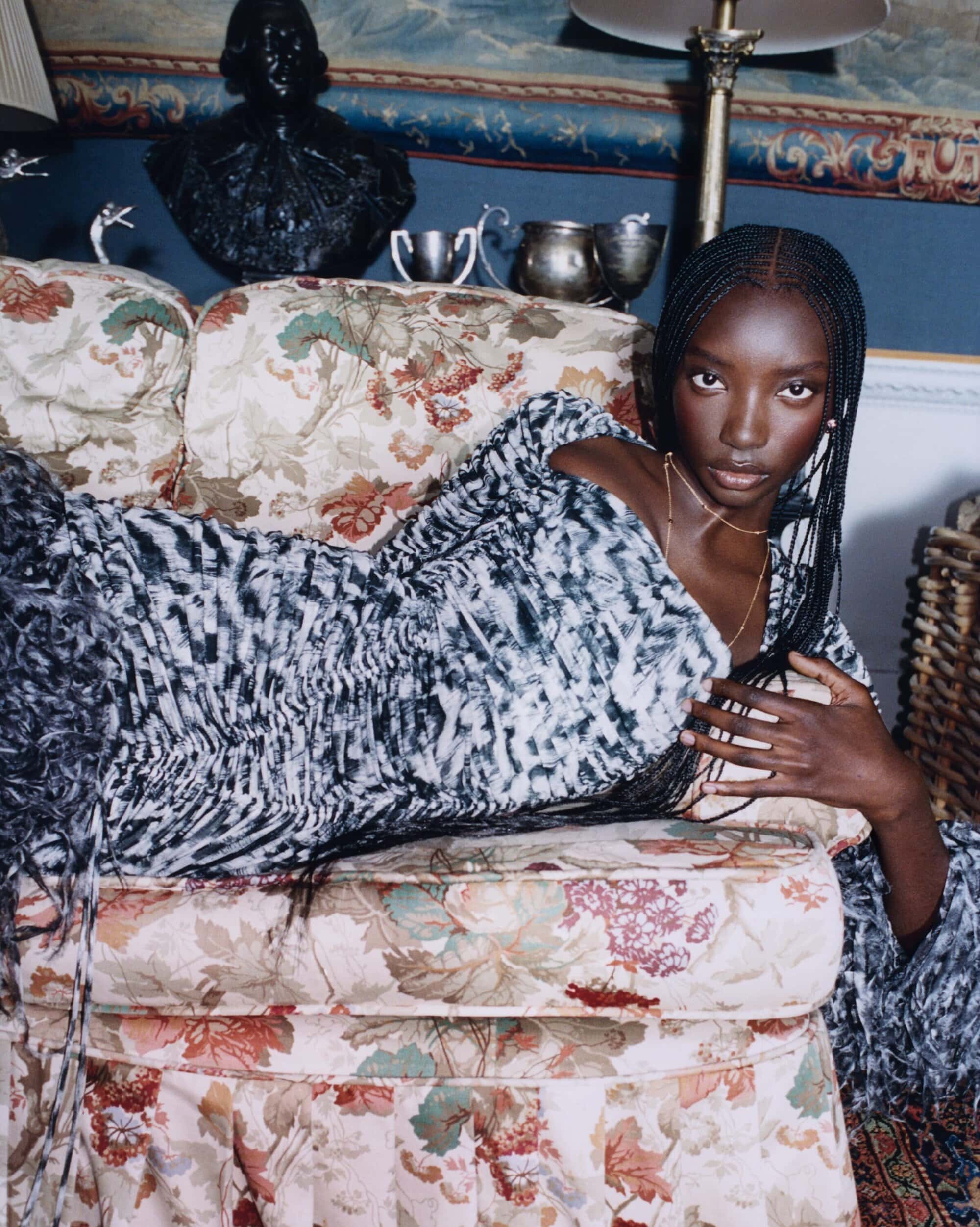 Model reclining on a floral patterned sofa in a dark interior setting for Burberry Fall 2025 campaign