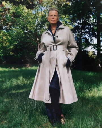 Model standing outdoors in a park wearing a beige belted trench coat over dark clothing, shot by Sam Rock for Burberry.