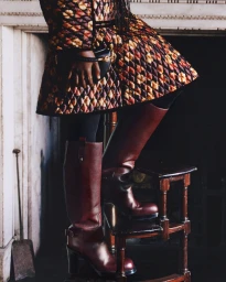 Model wearing a diamond-quilted floral jacket and tall burgundy boots standing on wooden step stool