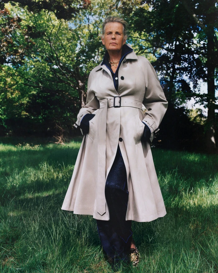 Model standing outdoors in a park wearing a beige belted trench coat over dark clothing, shot by Sam Rock for Burberry.