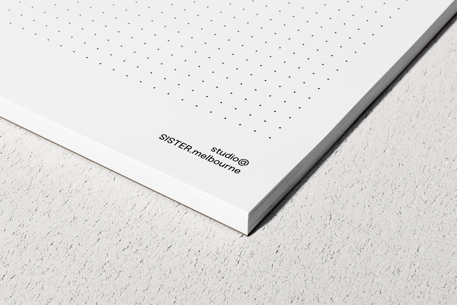 Close-up of a stack of dotted paper notebooks resting on a textured grey surface with printed branding text.