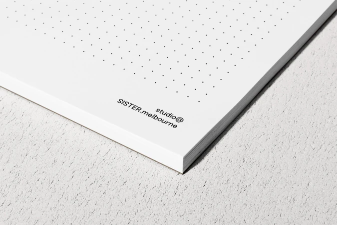 Close-up of a stack of dotted paper notebooks resting on a textured grey surface with printed branding text.