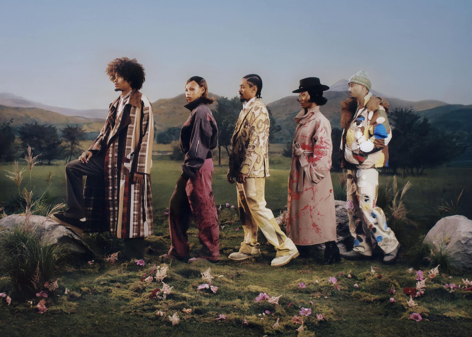 Five models in patterned and textured outerwear posing in a grassy landscape with rolling hills for KidSuper Fall 2025 campaign