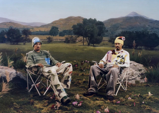 Two men seated in camping chairs on a grassy landscape with rolling hills in the background for the KidSuper fall 2025 ad campaign