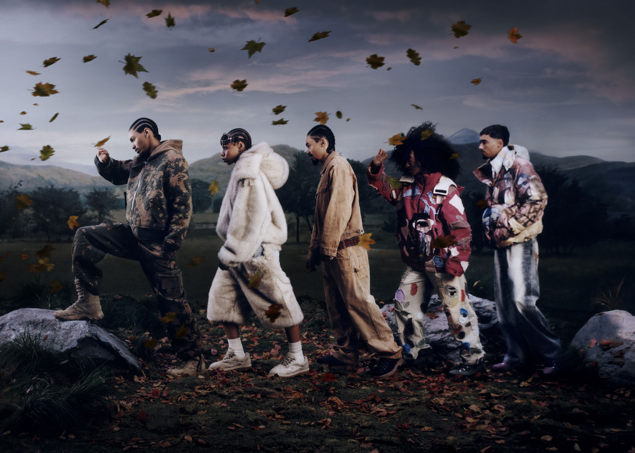 Group of models in styled outerwear walking through an autumn landscape with falling leaves under a moody sky