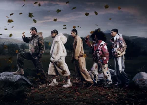 Group of models in styled outerwear walking through an autumn landscape with falling leaves under a moody sky