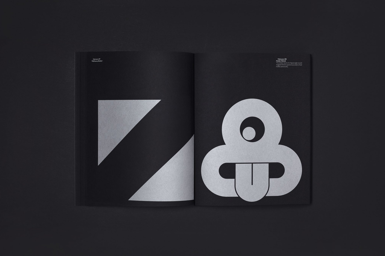 Open black catalog showing silver geometric shapes and typographic layouts on dark pages