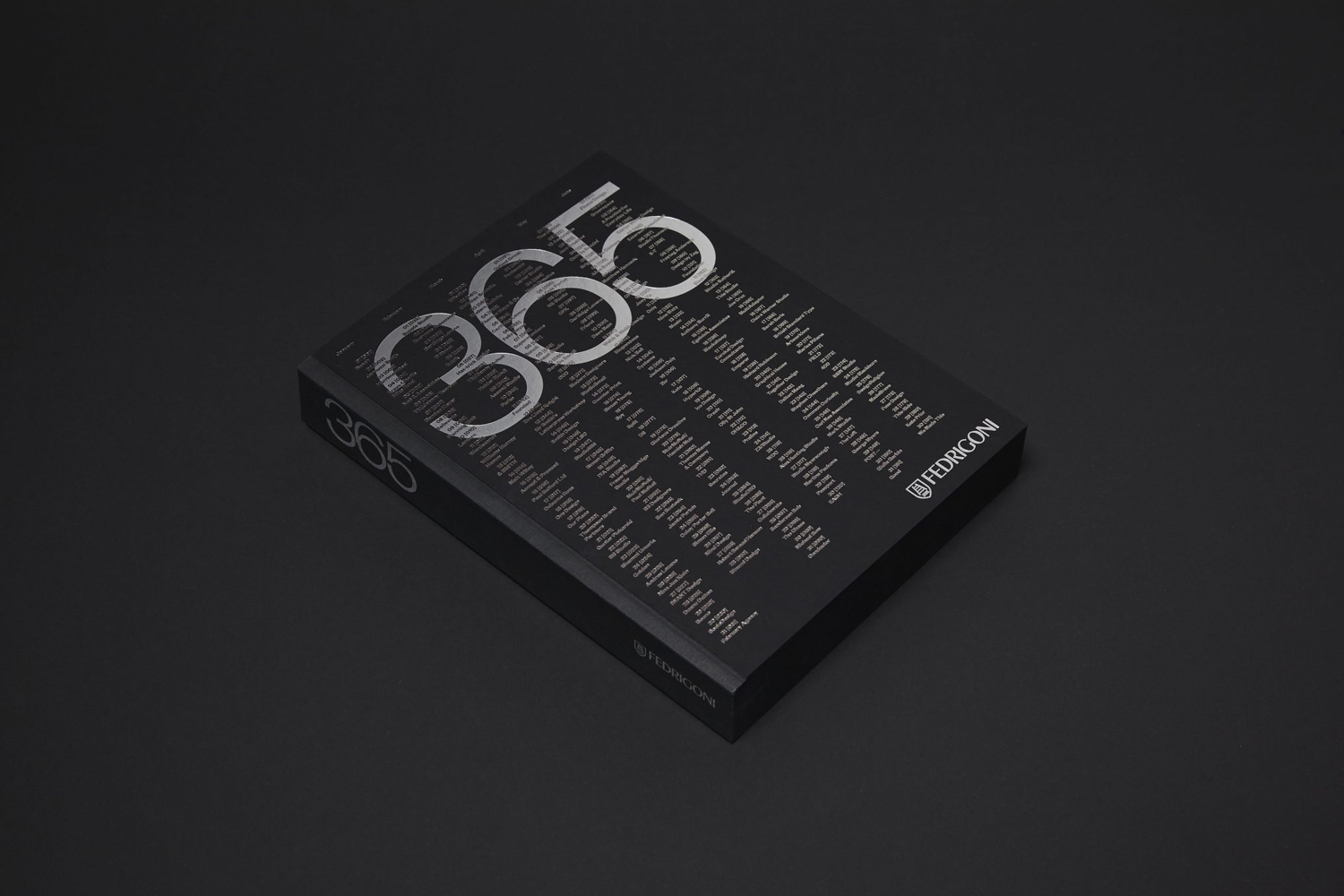 A black book with silver typographic numbers 365 on the cover resting on a dark surface for Fedrigoni brand identity.