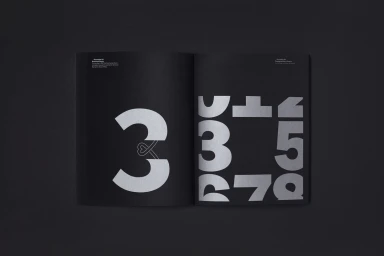 Open black booklet displaying large silver typography numerals on dark matte pages