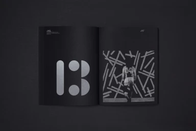 Open black catalog showing large silver typography on the left page and a graphic illustration on the right.