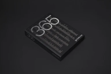 A black book with the number 365 printed in large silver typography on the cover, resting on a dark surface.