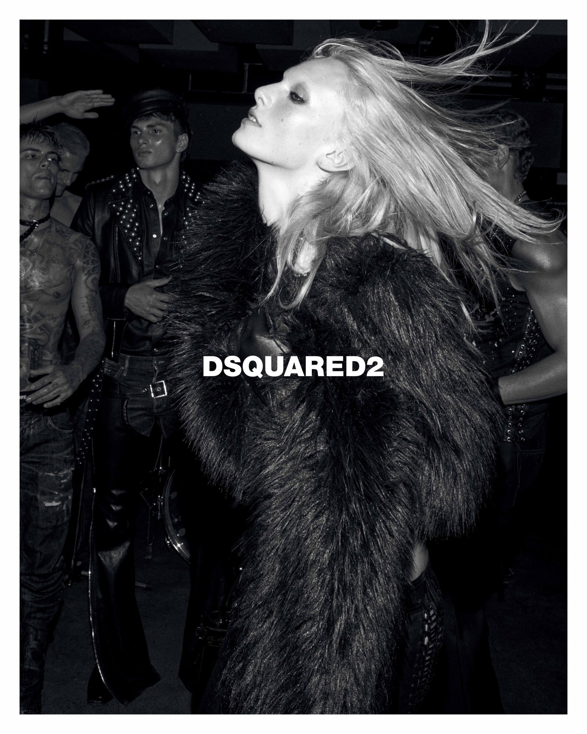 Black and white editorial fashion campaign shot featuring a model with long flowing hair wearing a dark faux fur coat.