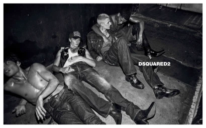 Monochrome campaign image of four young male models lounging on a dark concrete floor wearing denim and leather boots for Dsquared2.