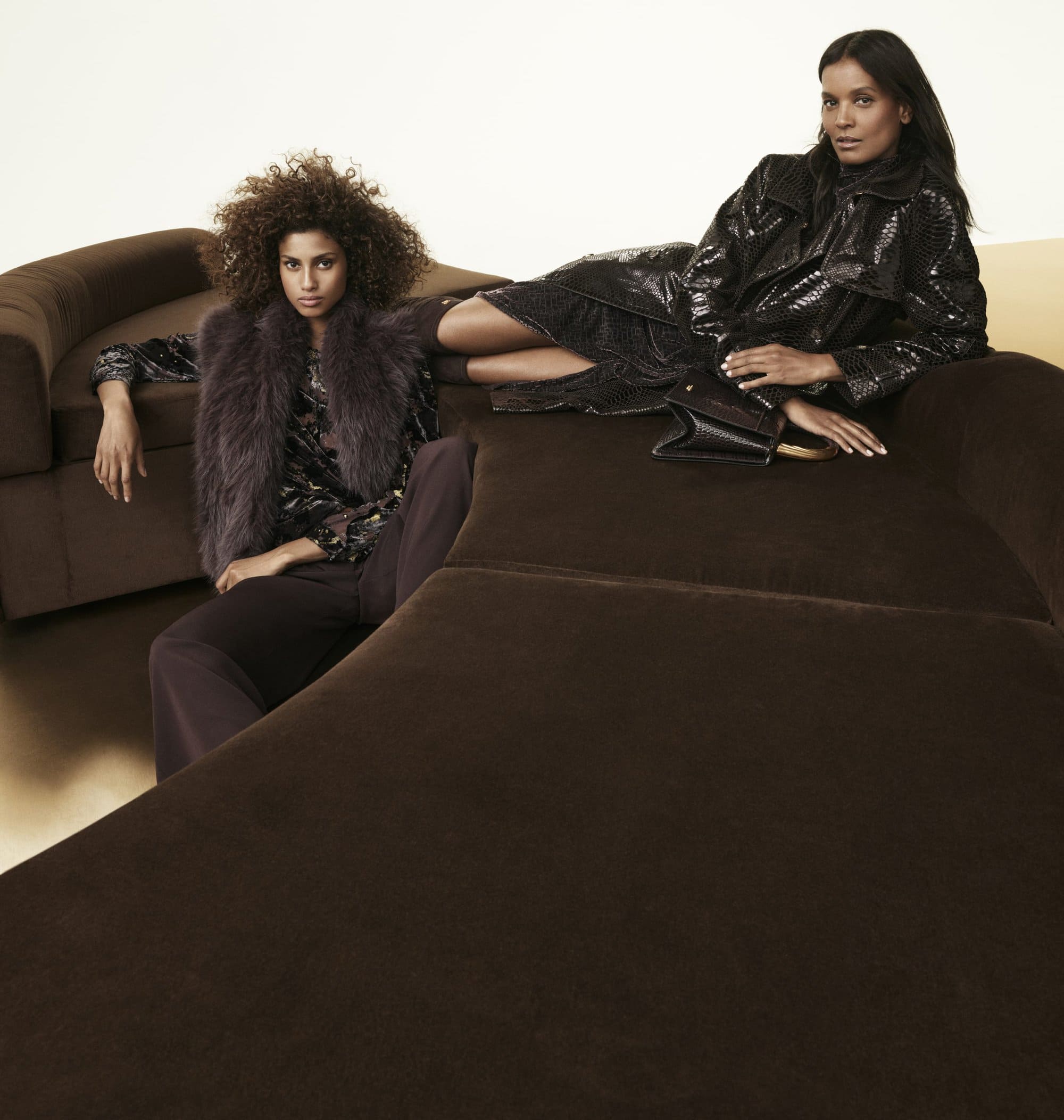 Two female models posing on a dark brown velvet sofa for the Donna Karan Fall 2025 ad campaign photographed by Mikael Jansson