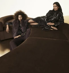 Two female models posing on a dark brown velvet sofa for the Donna Karan Fall 2025 ad campaign photographed by Mikael Jansson