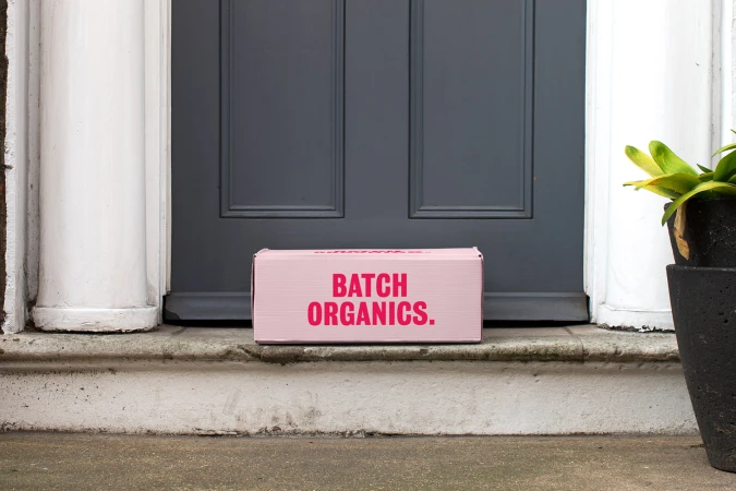 Pink Batch Organics delivery box placed on a stone doorstep in front of a dark grey front door with white pillars