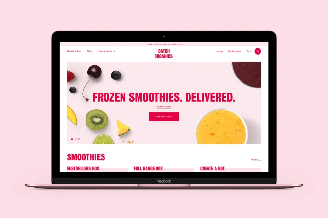 A laptop displaying the Batch Organics website with pink branding and fresh fruit imagery against a matching pink background.
