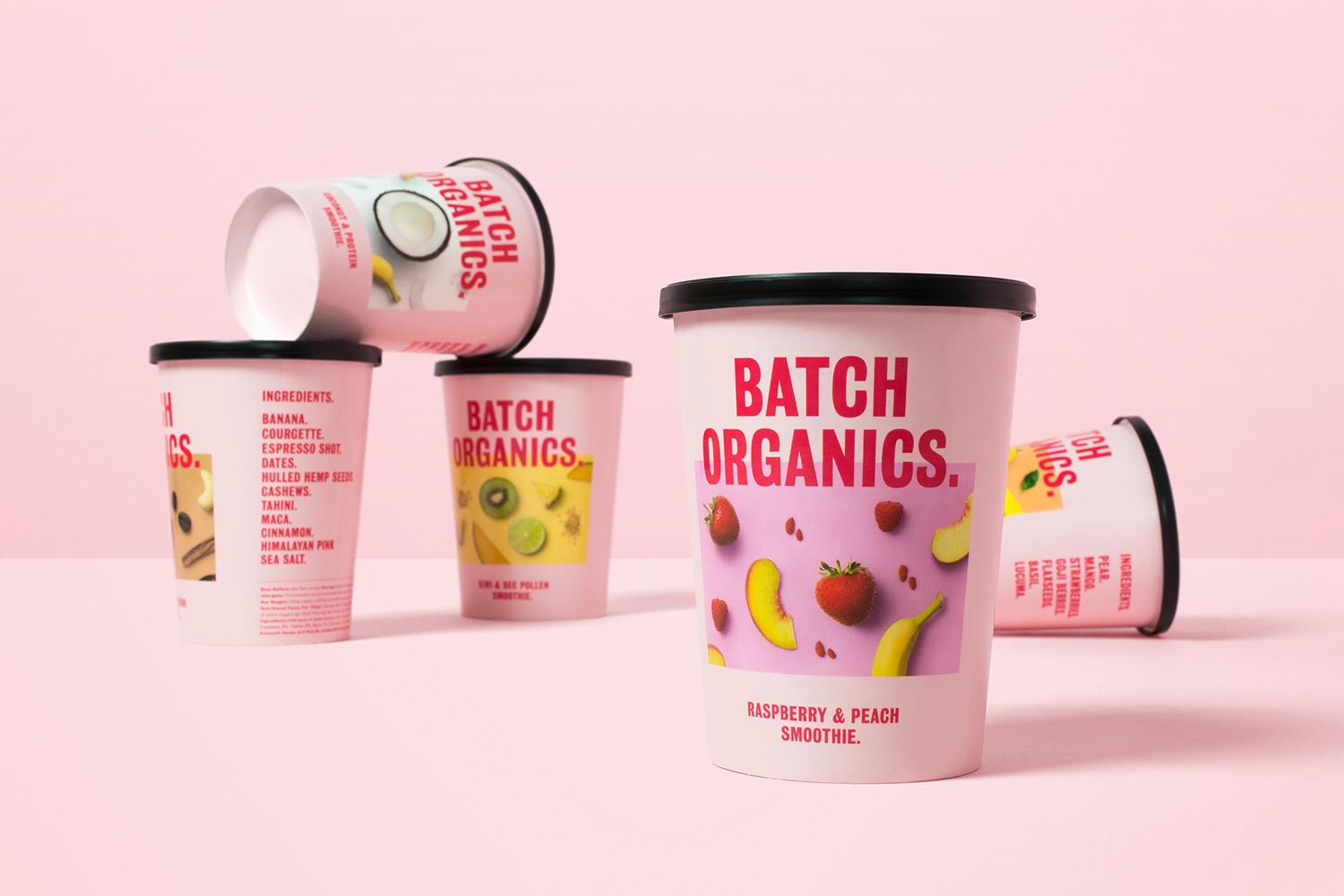 Several pink smoothie cups with black lids arranged on a pink surface featuring bold typography and fruit graphics.