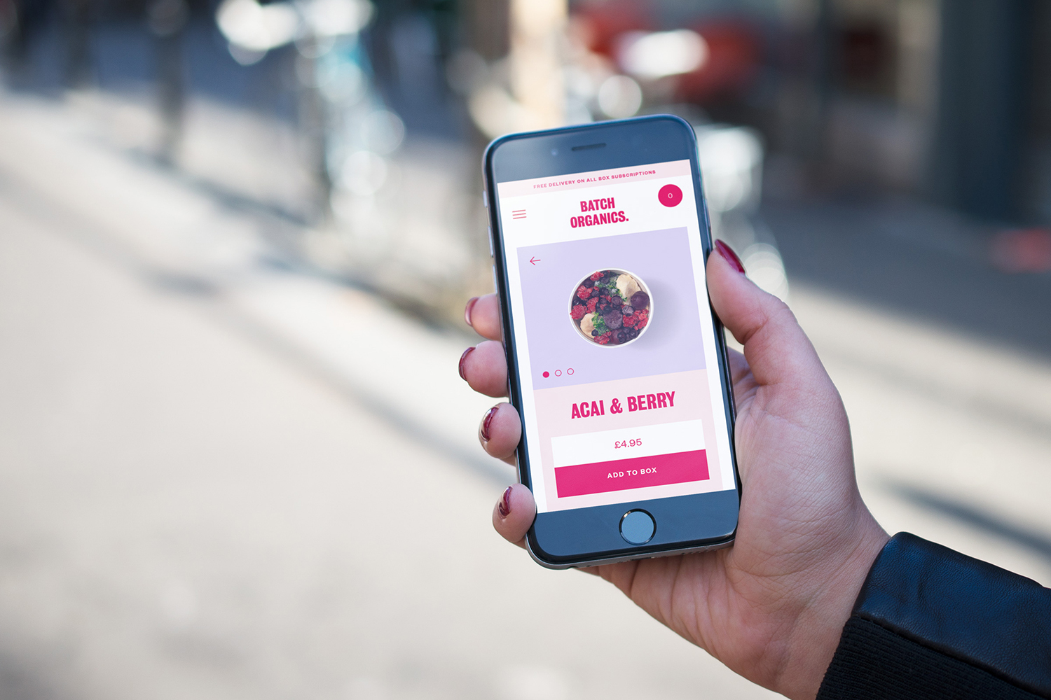 Hand holding a smartphone displaying the Batch Organics mobile app interface outdoors with a blurred street background.