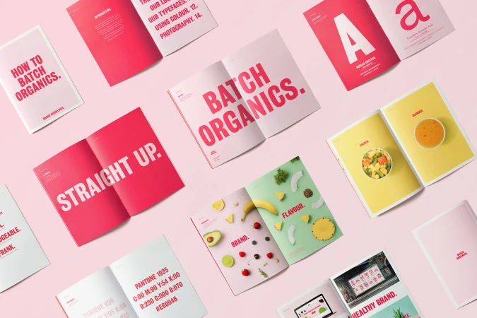 Flat lay photograph showing multiple open brand guideline booklets with pink, yellow, and green pages on a pale pink surface.