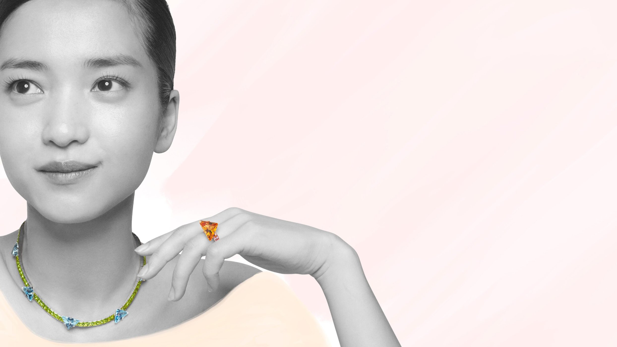 Close-up portrait of an East Asian woman wearing a gemstone necklace and ring against a pale backdrop for Prada campaign.
