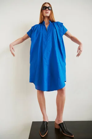 Model wearing a bright blue dress and black mules standing against a plain light wall for Zero + Maria Cornejo Pre-Fall 2025.