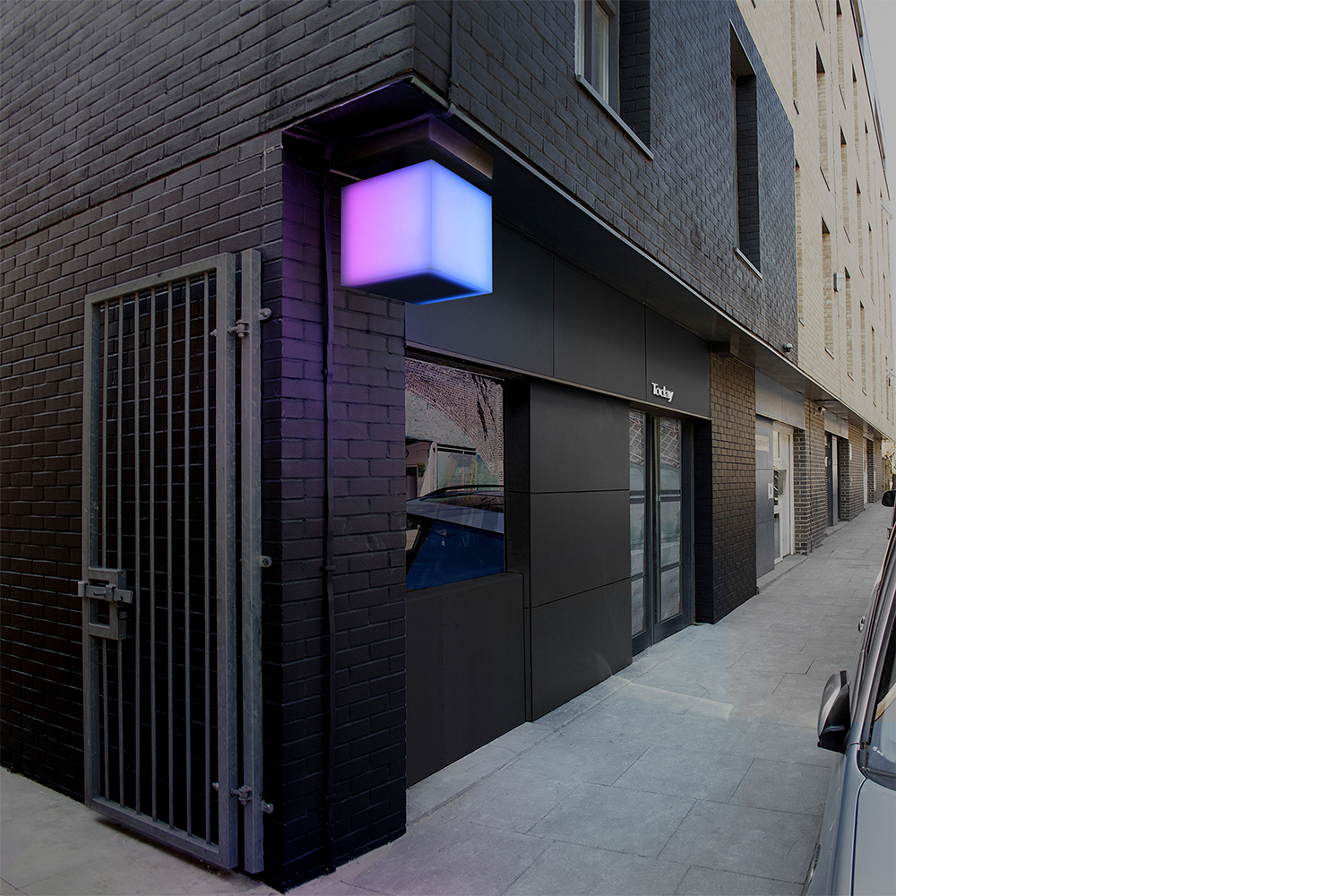 Exterior view of a modern building with a dark brick facade, a glowing pink and blue cube light fixture, and a storefront sign reading Today.