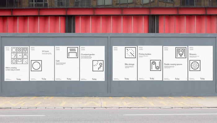 Monochrome graphic posters with minimalist icons mounted on a grey construction hoarding below red beams.
