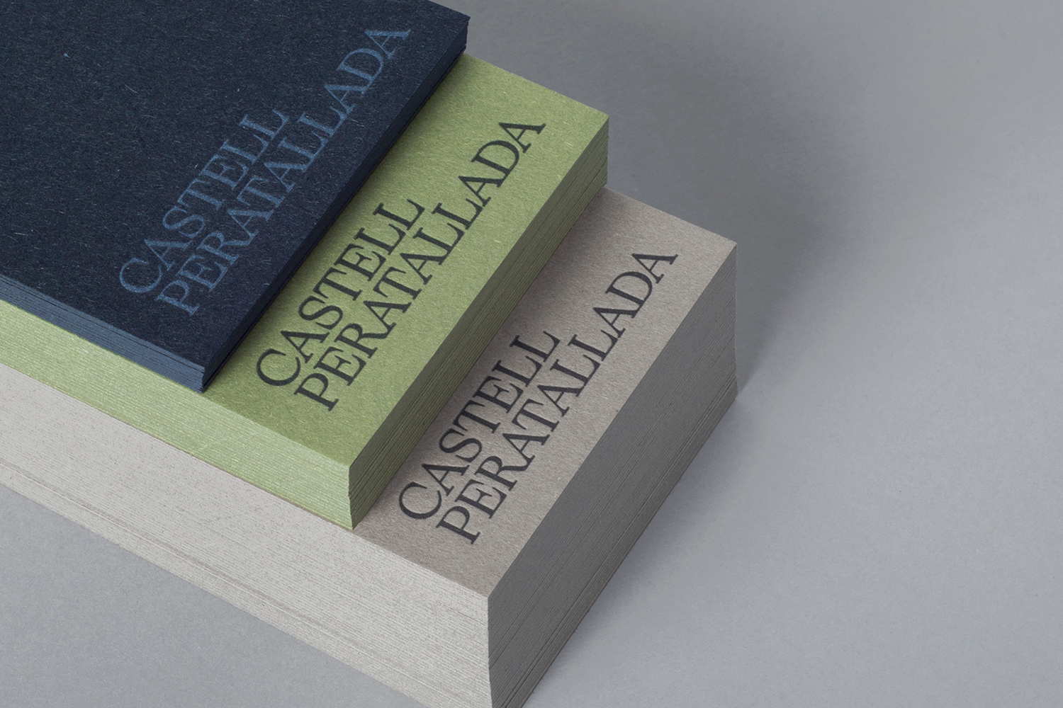 Stacked business cards in navy blue, pale green, and grey with embossed typography resting on a neutral background.
