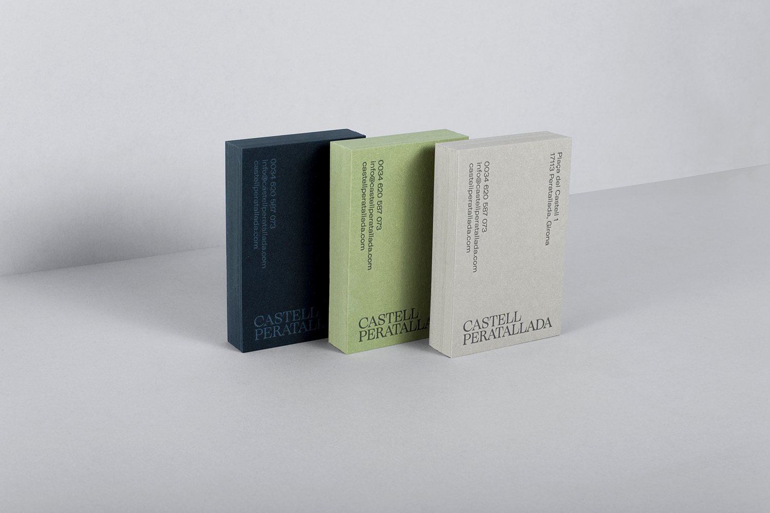 Three thick stacked business card sets in dark blue, light green, and cream resting on a white seamless background.