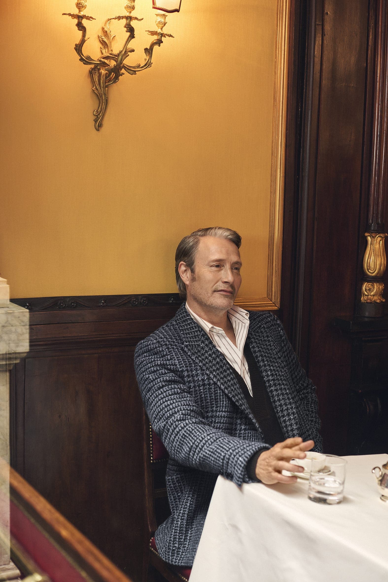 Mads Mikkelsen wearing a patterned blue blazer seated at a table for Zegna Fall 2025 ad campaign.