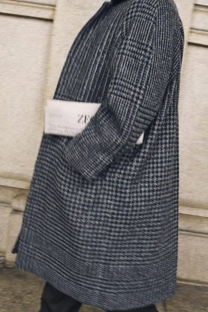 Close-up of Mads Mikkelsen wearing a grey houndstooth patterned coat holding a newspaper for Zegna Fall 2025 ad campaign.
