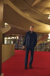Actor Mads Mikkelsen standing on a bright red carpet inside a grand modern architectural interior for Zegna Fall 2025 campaign.