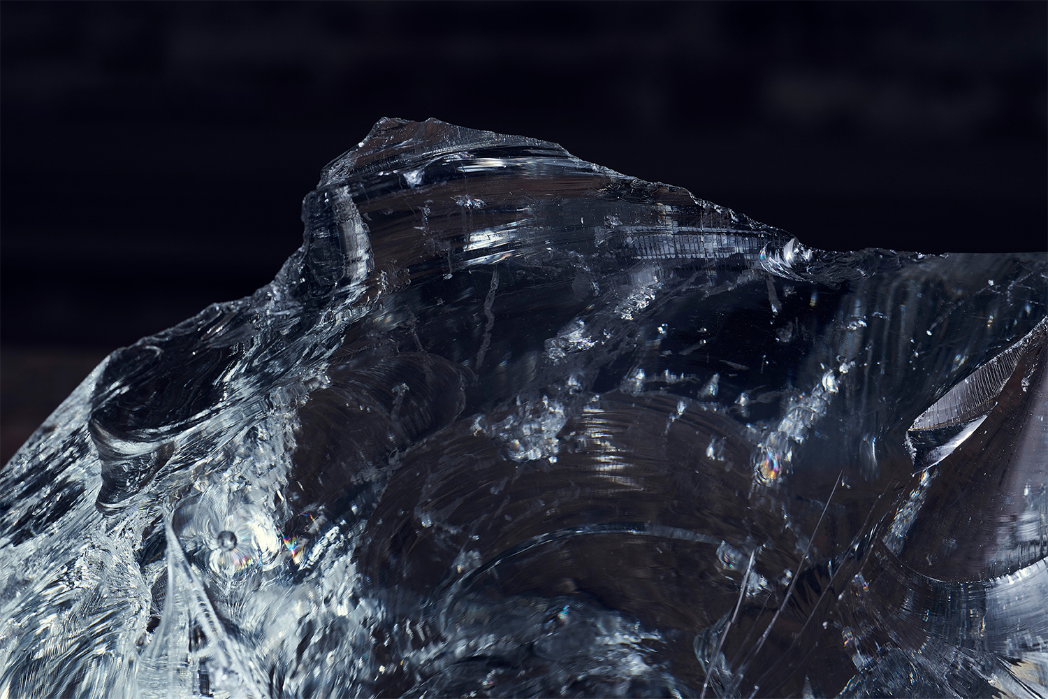 Close up macro view of rough translucent glass rock with sharp facets and internal fractures against dark background