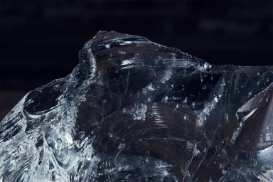 Close up macro view of rough translucent glass rock with sharp facets and internal fractures against dark background